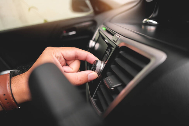 Το χέρι του οδηγού ρυθμίζει την ένταση στο ταμπλό του αυτοκινήτου ραδιόφωνο. - Φωτογραφία, εικόνα