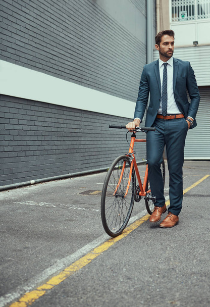 Doing his bit to leave a cleaner footprint. a handsome young businessman standing alongside his bike outdoors - Foto, immagini