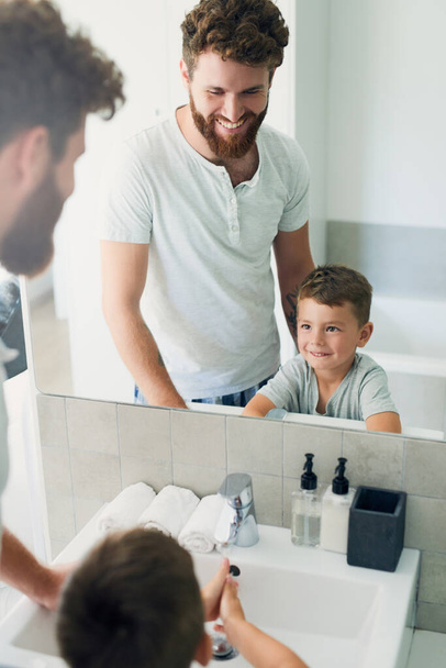Ξεκινήστε τη μέρα σας με καθαριότητα. Ένας νεαρός όμορφος πατέρας που βοηθάει το αξιολάτρευτο αγοράκι του να πλύνει τα χέρια του στο μπάνιο στο σπίτι. - Φωτογραφία, εικόνα