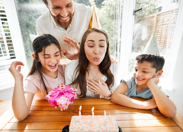Birthday, family and celebration with a woman blowing the candles on her cake. Husband and kids spoiling mom and making her feel happy on her special day mothers day while having a party at home. - Fotoğraf, Görsel