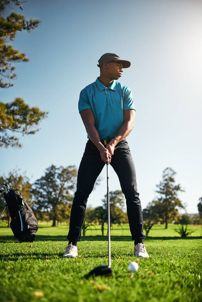 Смотрю, куда пойдет мяч. сфокусированный молодой мужчина-гольфист собирается качаться и играть в гольф со своей клюшкой снаружи на поле - Фото, изображение