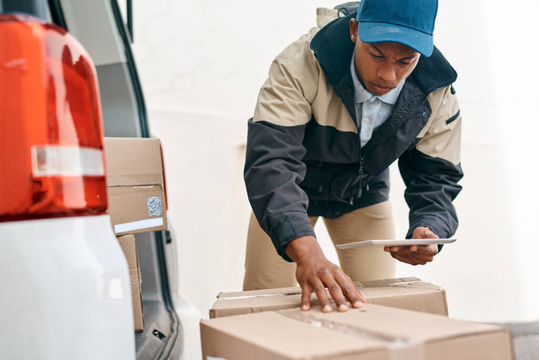 Double-checking his orders for delivery. a courier using a digital tablet while sorting boxes from a delivery van - Foto, immagini