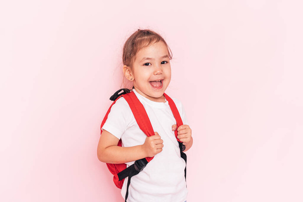 Laughing little girl with a red briefcase stands in front of a pink background. - Фото, зображення