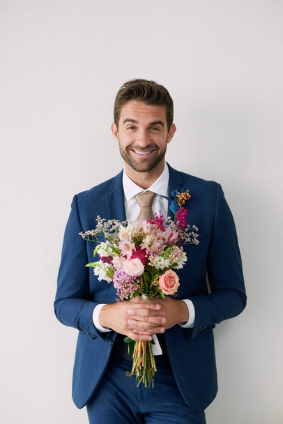 Theyre beautiful but not as beautiful as my bride. Studio shot of a handsome young groom holding a bunch of flowers a gray background - Φωτογραφία, εικόνα