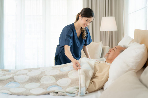 Азійська медсестра, яка доглядає за домом, підтримує літнього чоловіка, який спить на ліжку у палаті пацієнта. - Фото, зображення