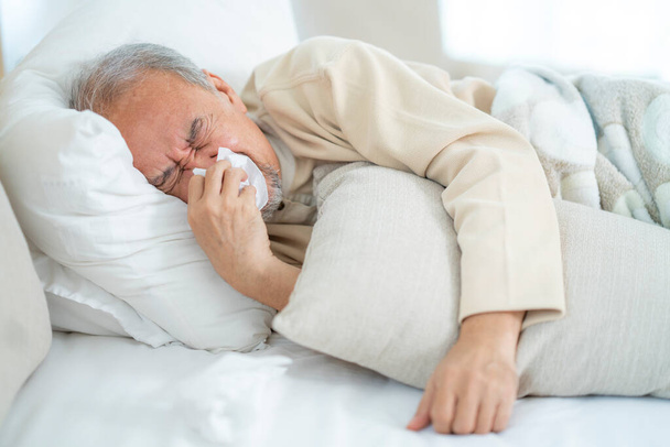 Ein alter Mann hat einen coviren Virus und nimmt Quarantäne auf dem Bett in seinem Haus. Alter Mann hustet und schläft auf dem Bett. - Foto, Bild