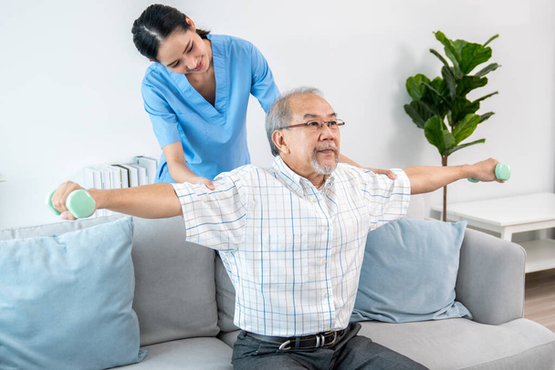 Contented senior patient doing physical therapy with the help of his caregiver. Senior physical therapy, physiotherapy treatment, nursing home for the elderly - Valokuva, kuva