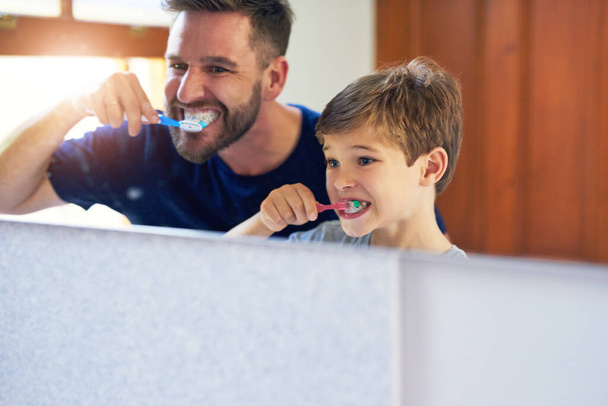 Вгору, вниз, вгору, вниз, вгору і вгору. батько і його маленький син чистять зуби разом вдома
 - Фото, зображення