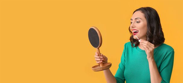 Beautiful young woman applying makeup on yellow background with space for text - Photo, Image