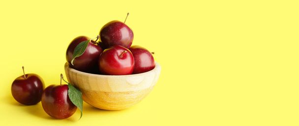 Bowl of fresh ripe plums on yellow background with space for text - 写真・画像