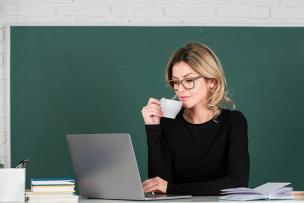 Portrait of teacher or female tutor working at table and drinking coffee in college or high school. Young women student studying in class - Foto, Bild