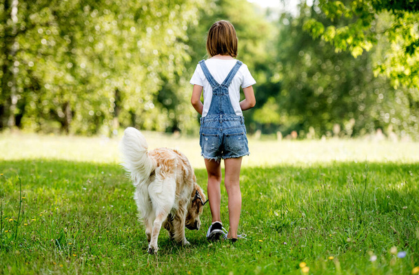 Rear view of a little girl walking dog on flowering meadow. Back view - Valokuva, kuva
