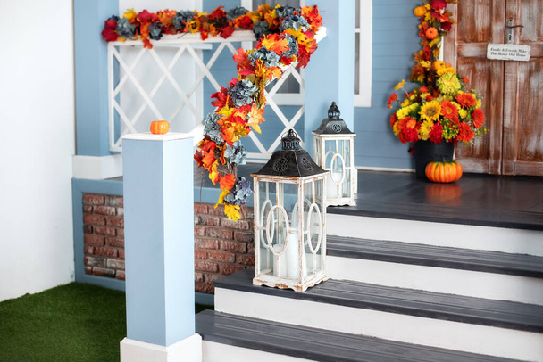 Cozy porch of the house with wooden lanterns in fall time. Halloween design home with yellow fall leaves and lamps. House entrance staircase decorated for autumn holidays, fall flowers and pumpkins.  - Foto, Bild