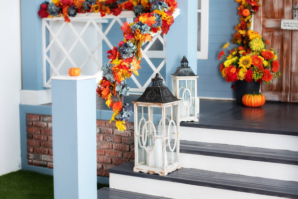 Cozy porch of the house with wooden lanterns in fall time. Halloween design home with yellow fall leaves and lamps. House entrance staircase decorated for autumn holidays, fall flowers and pumpkins.  - Foto, Bild