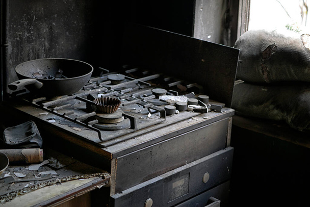 A flat in the town of Borodyanka after being hit by a shell. A burned electric cooker, cracked wall and ashes from furniture, burnt flowers and children's shoes. - Foto, afbeelding