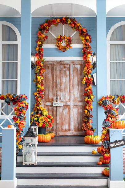 House entrance staircase decorated for autumn holidays, fall flowers and pumpkins. Cozy wooden porch of the house with pumpkins in fall time. Halloween design home with yellow fall leaves and lanterns - Photo, Image