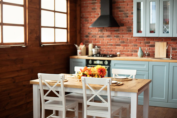  Cozy cuisine decorated with fall decor and table setting flowers and pumpkins. Interior design scandinavian kitchen with utensils, dishes, plates. Stylish dining room with wooden table and chairs. - Foto, Imagem