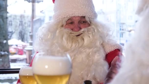 Friends in Santa Claus costumes are having fun at a New Years party, drinking beer in a pub. Celebration of Christmas and New Year 2023 - Felvétel, videó