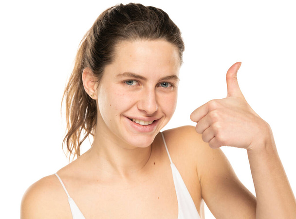 Portrait of a young smiling woman with tied hair and without makeup showing thumbs up on a white background. - Valokuva, kuva