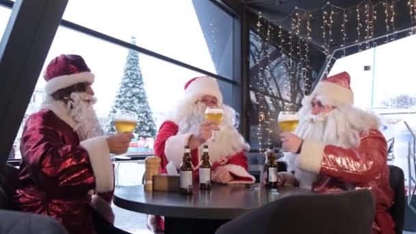 Друзья в костюмах Санта Клауса веселятся на новогодней вечеринке, пьют пиво в пабе. Празднование Рождества и Нового 2023 года - Кадры, видео