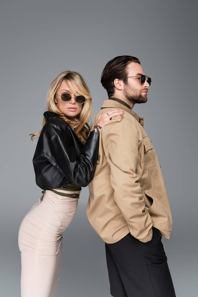 stylish blonde woman in sunglasses leaning on shoulders on bearded man isolated on grey - Foto, Bild