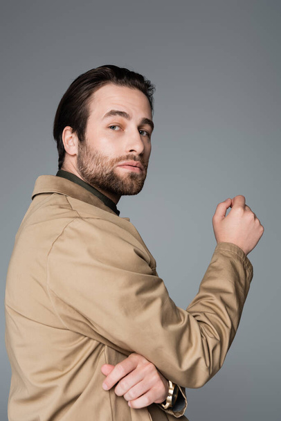 bearded man in beige jacket looking at camera isolated on grey - Zdjęcie, obraz