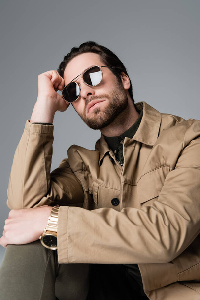 bearded man in stylish jacket and sunglasses looking at camera isolated on grey - Foto, Imagem