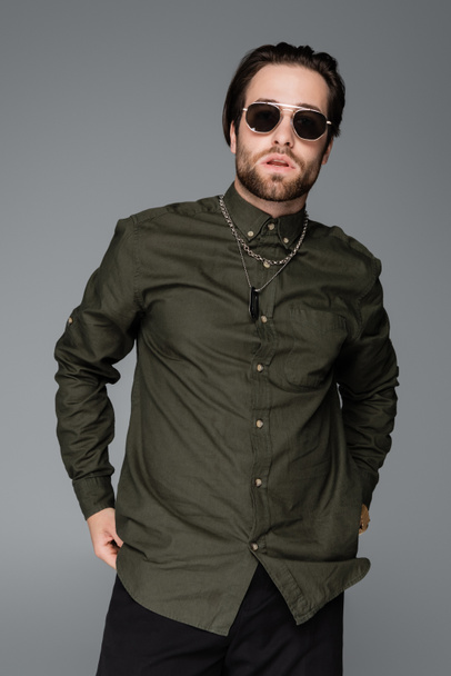 bearded man in stylish green shirt and sunglasses looking at camera isolated on grey - Fotó, kép