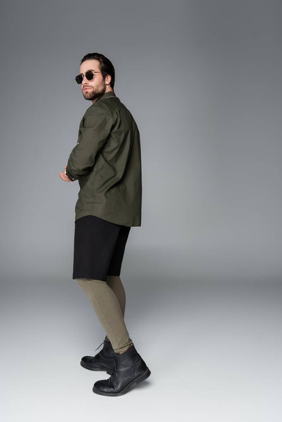 full length of bearded man in sunglasses and stylish outfit posing on grey - Fotoğraf, Görsel