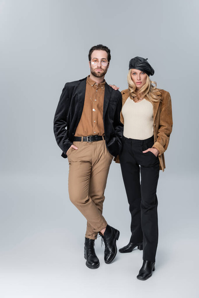 full length of blonde woman in stylish beret near bearded man in sunglasses posing on grey - Photo, Image