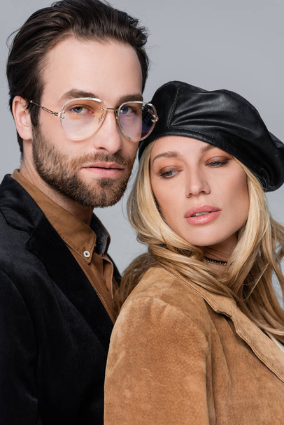 portrait of blonde woman in stylish beret near bearded man in sunglasses isolated on grey - 写真・画像