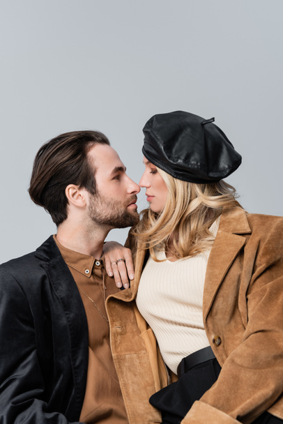 side view of blonde woman in stylish beret hugging bearded man isolated on grey - Photo, Image