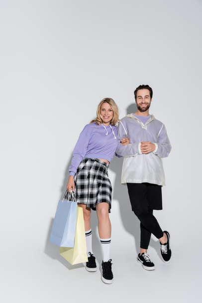 full length of happy and stylish couple holding shopping bags on grey - Фото, зображення