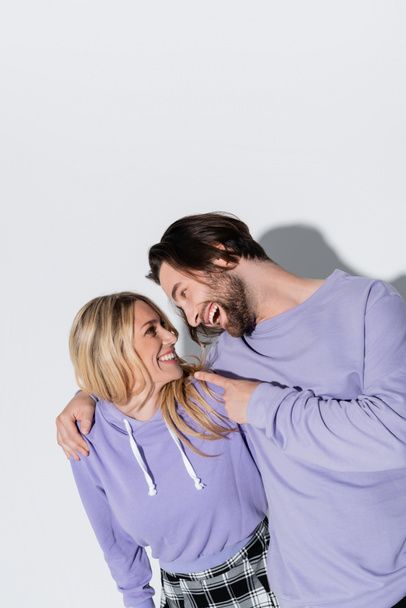 happy bearded man in purple sweatshirts pointing at blonde woman on grey - Fotoğraf, Görsel