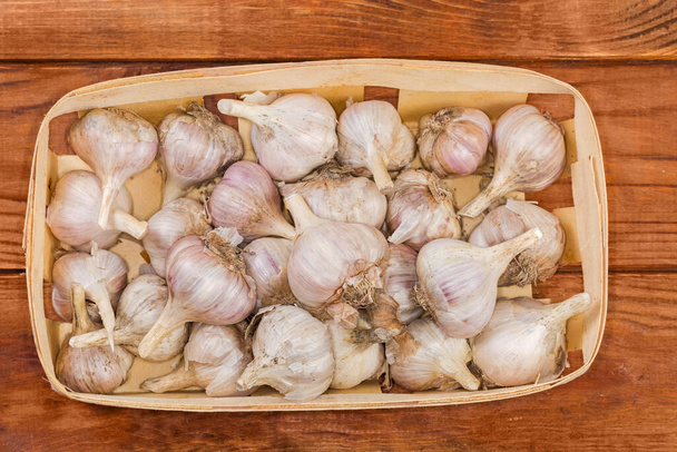 Freshly harvested heads of the purple garlic close-up in the small wooden basket on an old rustic table, top view - Foto, Bild