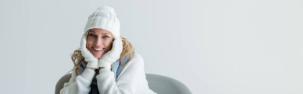 happy blonde woman in winter outfit and soft white gloves isolated on grey, banner - Photo, Image