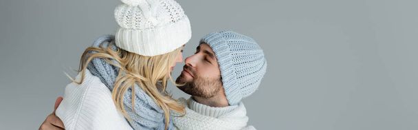blonde woman in knitted hat looking at bearded boyfriend in winter outfit isolated on grey, banner - Photo, Image