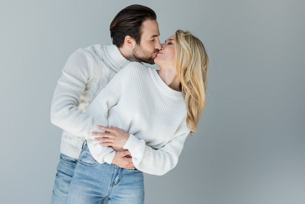bearded man and blonde woman in knitted sweaters kissing isolated on grey - Fotó, kép