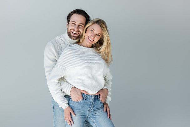 happy couple in white sweaters and denim jeans posing isolated on grey  - 写真・画像