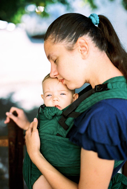 Mom hugging a baby in a baby carrier while standing in the garden. High quality photo - Valokuva, kuva
