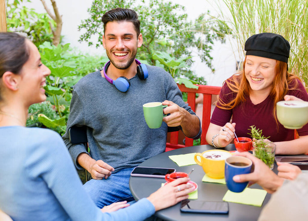 Υψηλή γωνία των χαρούμενων νέων ανδρών και γυναικών πίνοντας καφέ και γελώντας με αστείο, ενώ κάθεται γύρω από το τραπέζι κατά τη διάρκεια του διαλείμματος καφέ στον κήπο - Φωτογραφία, εικόνα