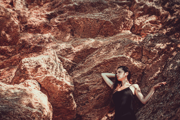 Girl in a black dress posing on a background of sand rocks - Foto, afbeelding