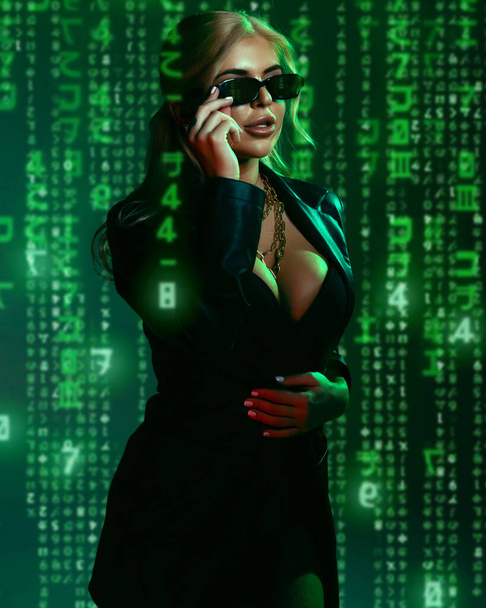 Gorgeous woman in matrix style suit. Black leather and reflection of code in glasses in green light and shadows of the matrix. Cyber technology concept, future and progress - Fotoğraf, Görsel