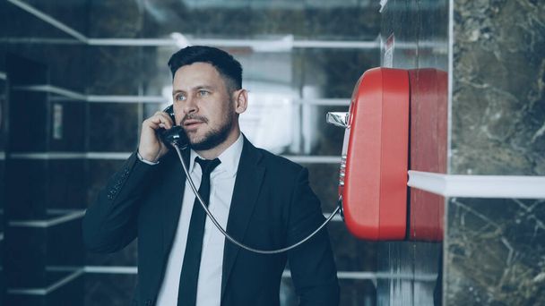 Bearded young businessman dial red telephone talking with staff at reception in hotel lobby. Business, travel and people concept - Foto, immagini