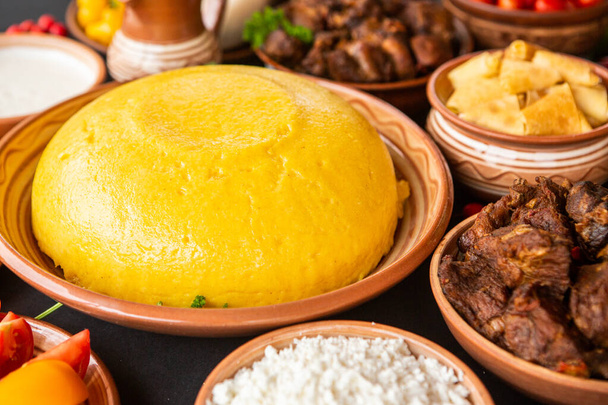 Homemade Romanian Food with polenta, meat, cheese and vegetables. Delicious corn porridge in clay dishes. Mamaliga or polenta, a traditional dish in Moldova, Hungary and Ukrainian cuisine. - Foto, afbeelding