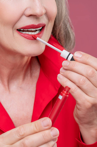 Lip gloss. Good-looking mature woman in red putting gloss on her lops - Valokuva, kuva