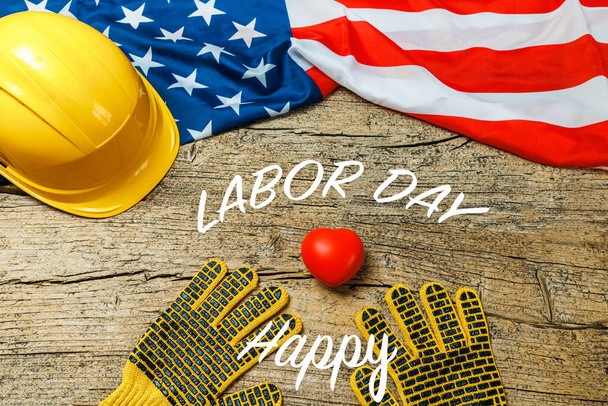 Αμερικανική απασχόληση στις κατασκευές, Πρωτομαγιά και βιομηχανική έννοια εργασίας με κοντά σε ένα κίτρινο σκληρό καπέλο και γάντια ασφαλείας με μικρή κόκκινη καρδιά κοντά στη σημαία των ΗΠΑ  - Φωτογραφία, εικόνα
