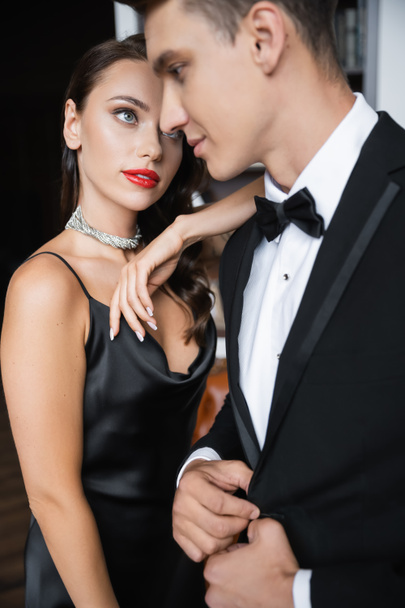 Brunette woman in silk dress looking at blurred boyfriend in suit at home  - Foto, Imagem