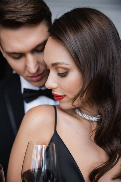 Brunette woman with red lips standing near boyfriend and glass of wine at home  - Photo, image
