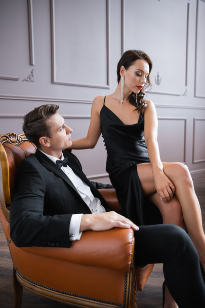 Elegant man looking at sensual girlfriend while sitting on armchair at home  - Foto, immagini